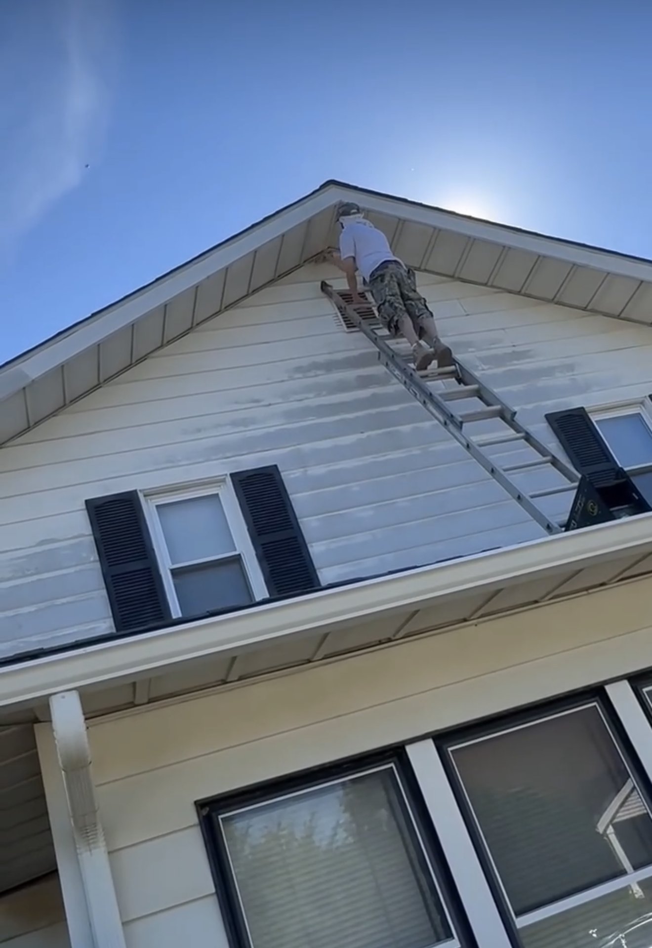 Painter on a ladder prepping a house gable