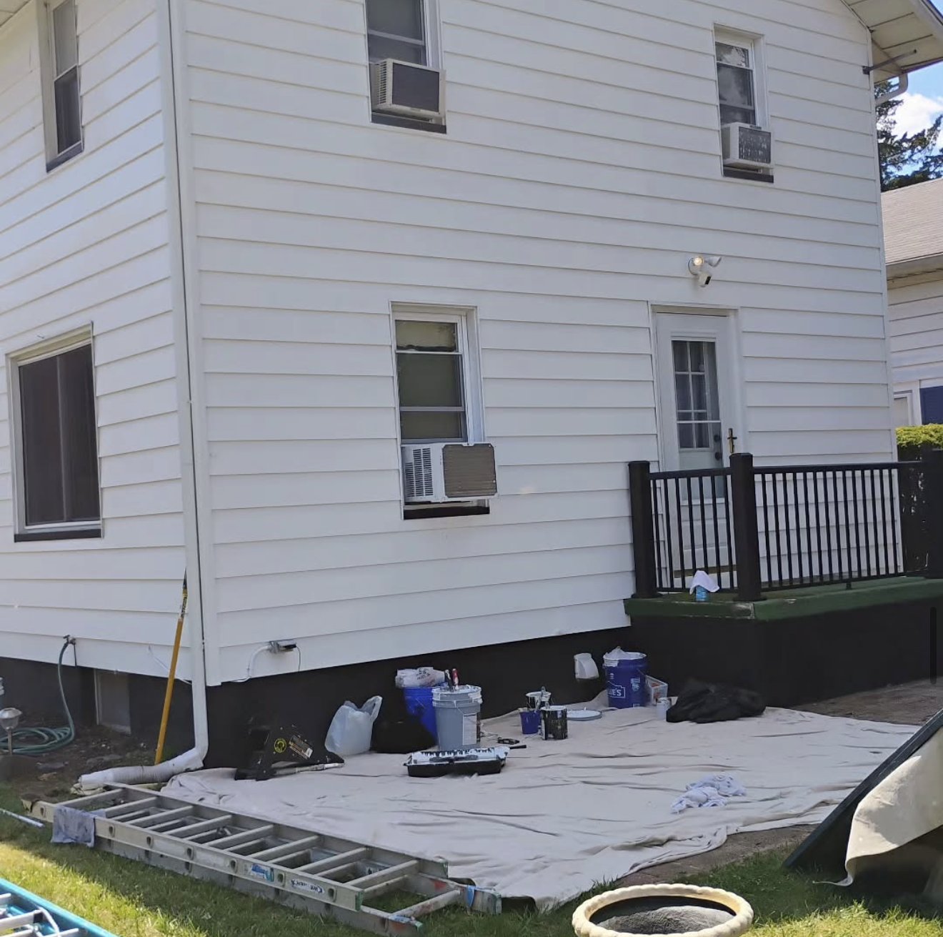 White siding house mid repaint with drop cloths down